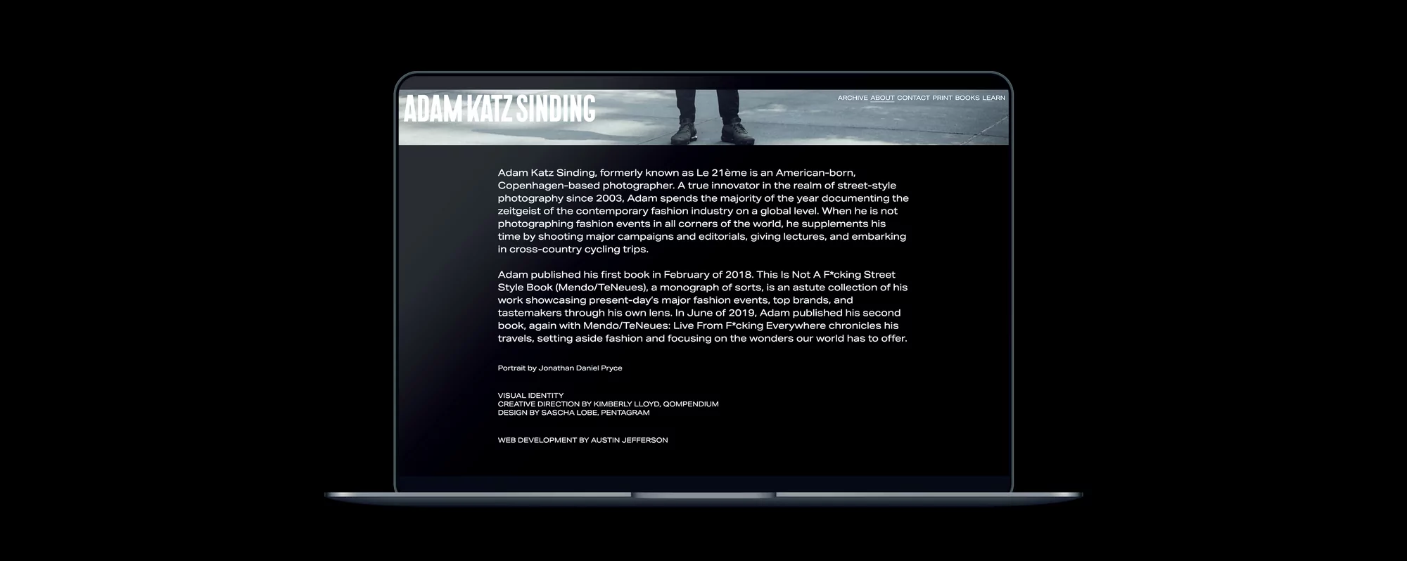 Laptop displays the website of photographer Adam Katz Sinding, featuring a black and white photo of the photographer's legs and shoes.