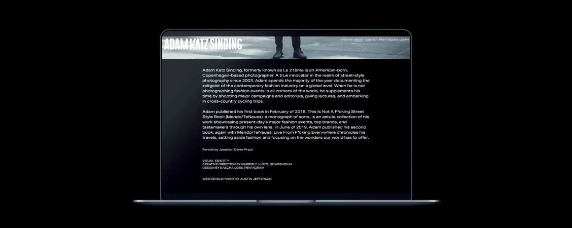 Laptop displays the website of photographer Adam Katz Sinding, featuring a black and white photo of the photographer's legs and shoes.