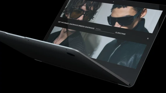 Laptop computer displaying website mockup featuring two men wearing sunglasses against a dark background