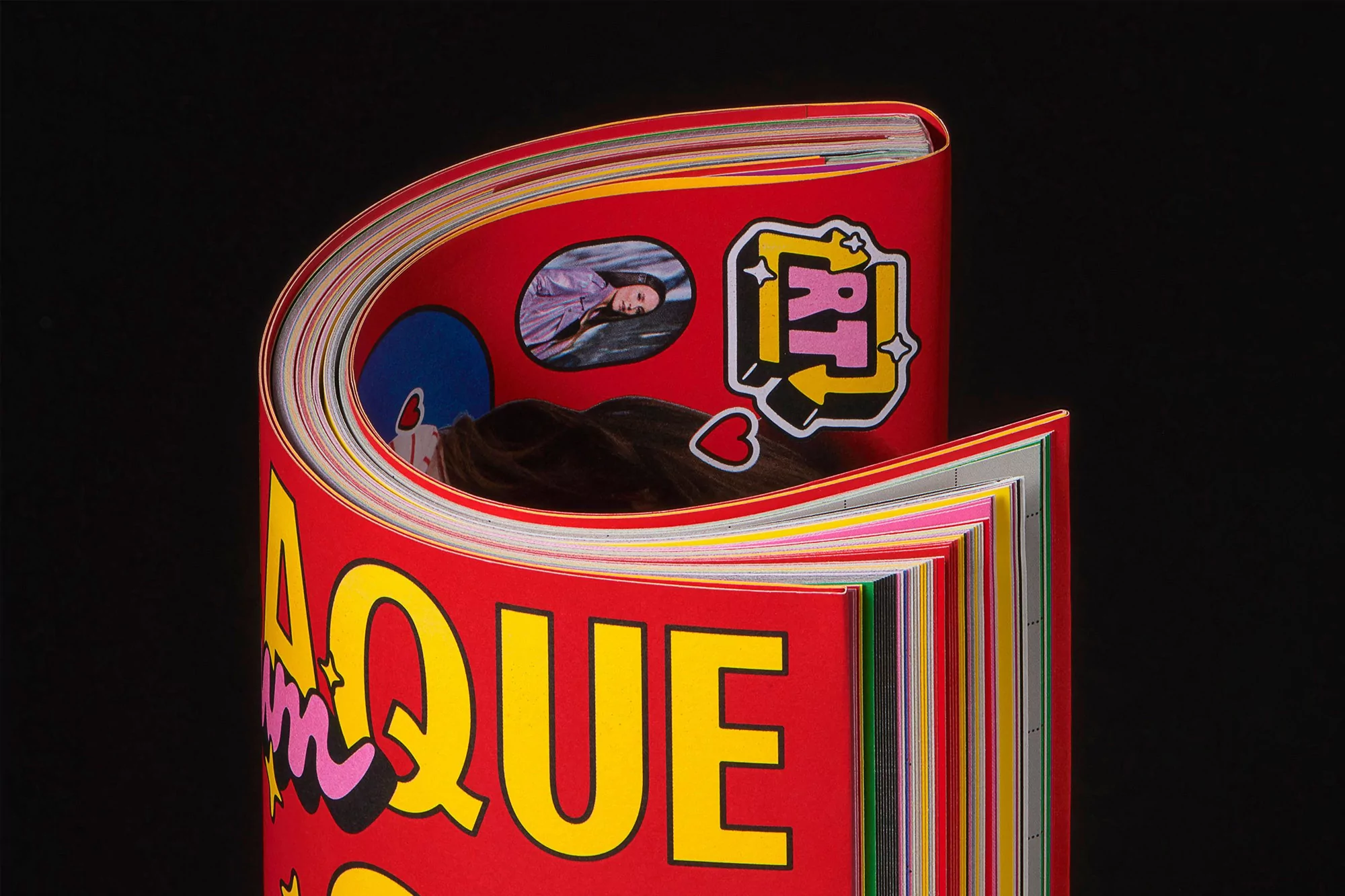 Close-up of a vividly colored magazine, opened to reveal vibrant imagery and bold typography, set against a stark black background.
