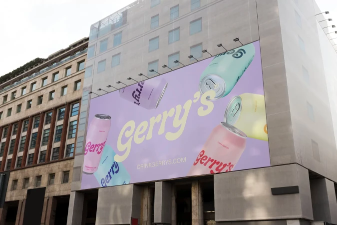 Outdoor advertisement featuring colorful Gerry's canned beverages on a building, promoting drinkgerrys.com, set against a city backdrop.