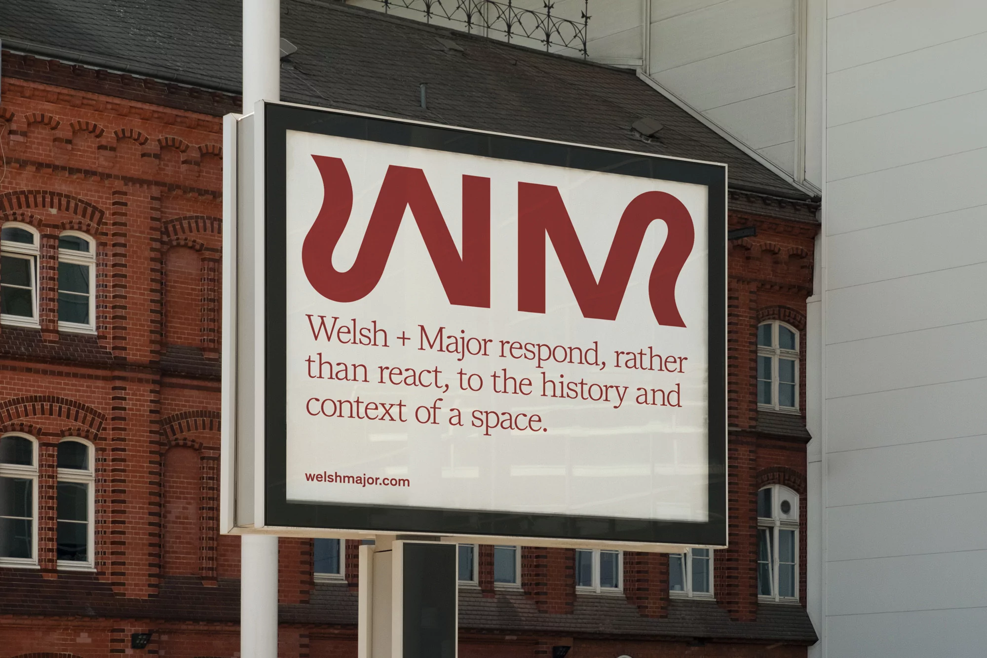 Outdoor advertisement for Welsh + Major featuring large red text on a white background, set against a brick building.