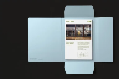 Open light blue presentation folder resting on a dark surface containing printed architectural documents for Welsh + Major