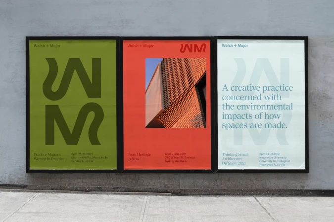Three architectural posters mounted in black frames on a grey textured concrete wall above a pavement.
