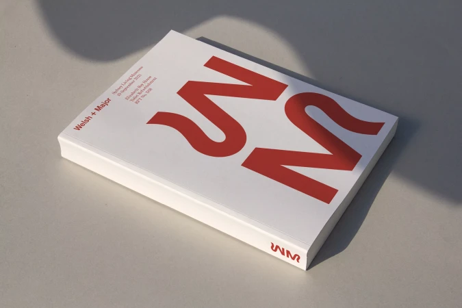 A white book with red branding and typography resting on a neutral grey surface under soft natural lighting