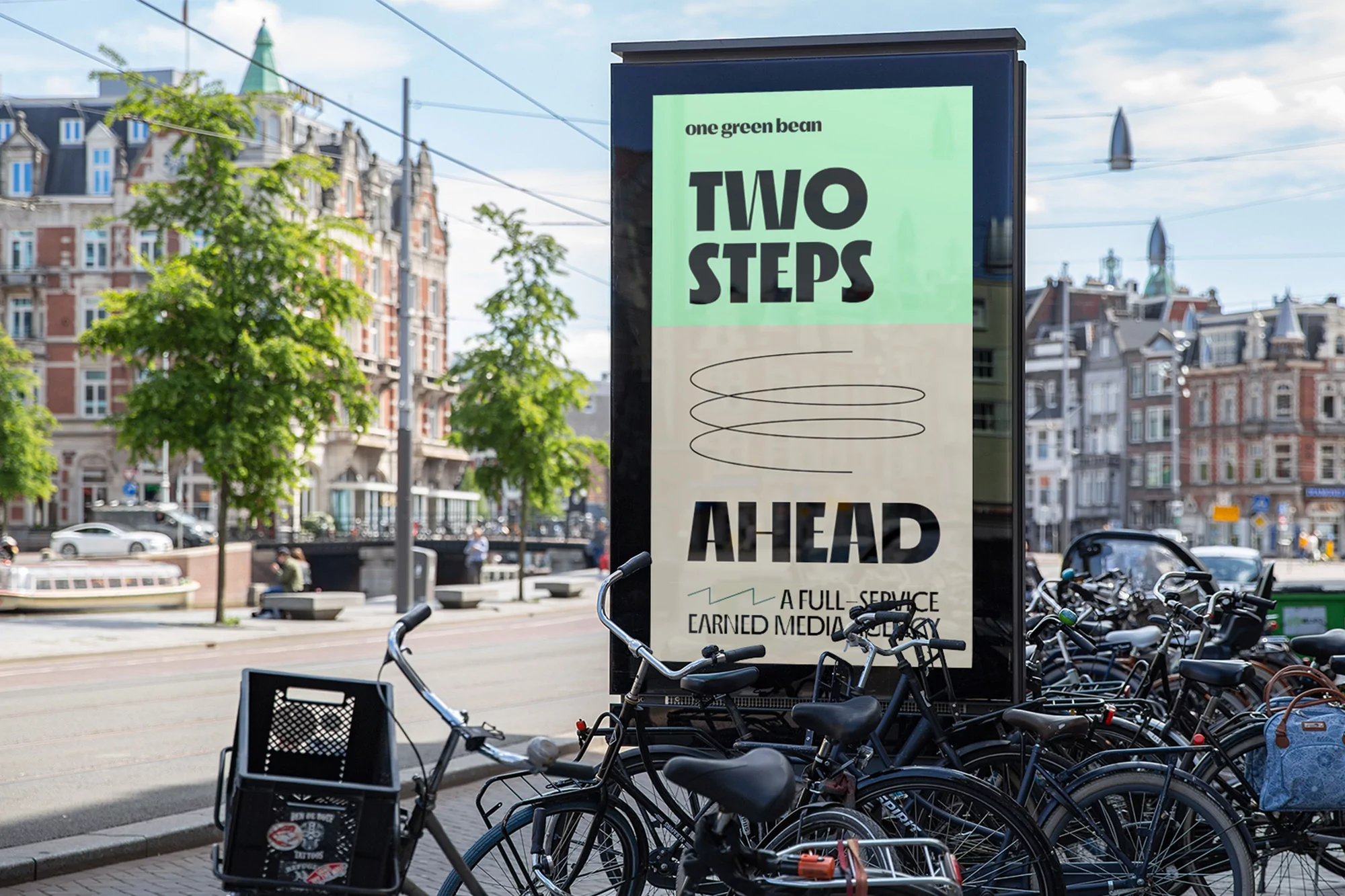 Outdoor billboard advertising 'One Green Bean Two Steps Ahead' with parked bicycles in the foreground in an urban setting.