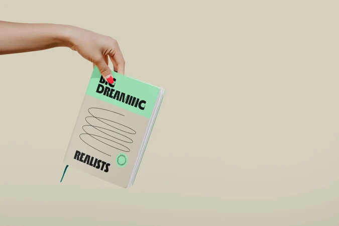 A woman's hand holds a book with a mint green stripe at the top, featuring bold black typography and minimalist design.