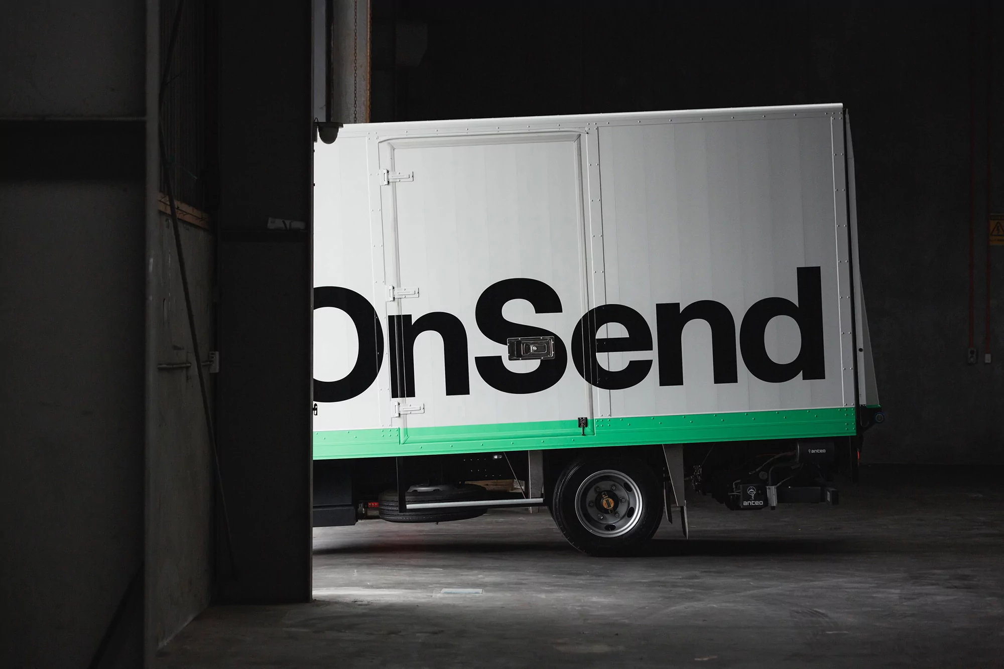 Delivery truck with the word 'OnSend' parked inside a loading dock, providing delivery and logistics in a warehouse setting.