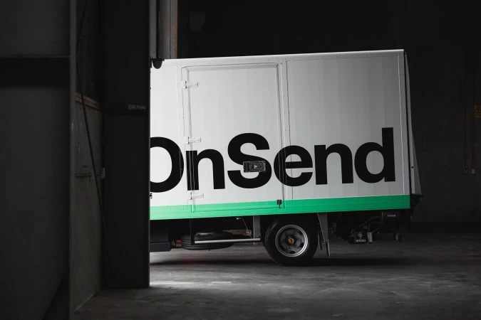 Delivery truck with the word 'OnSend' parked inside a loading dock, providing delivery and logistics in a warehouse setting.