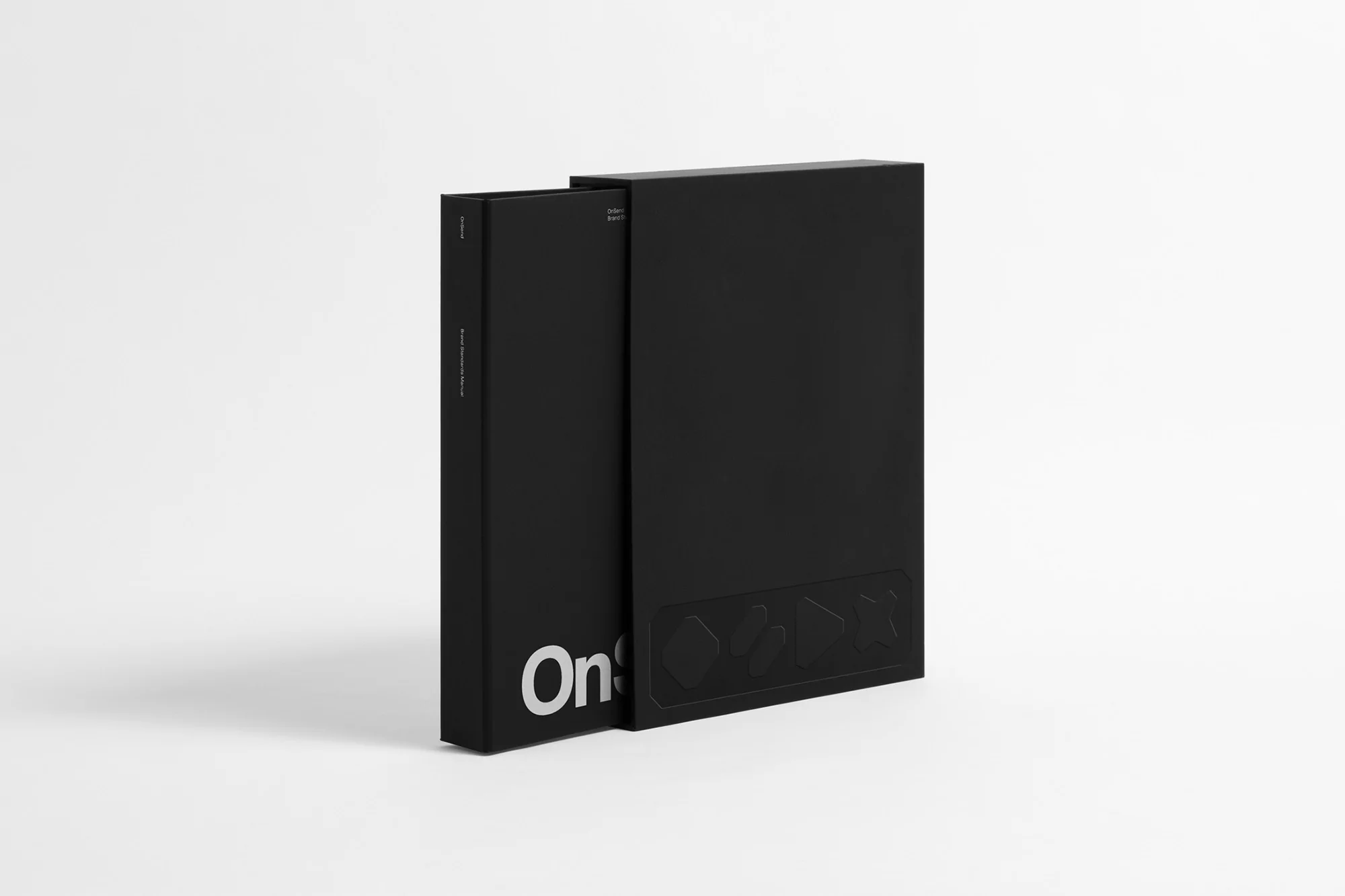 Studio shot of a black book sitting partially inside a black box on a white background. Geometric shapes are embossed on the box.