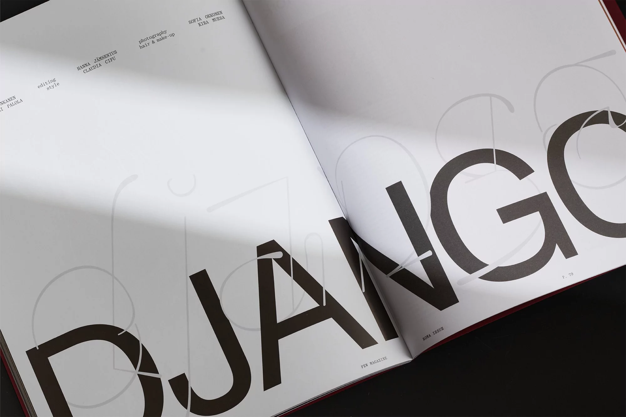 Open magazine spread on dark surface showing large typography spelling DJANGO with soft shadow across white pages