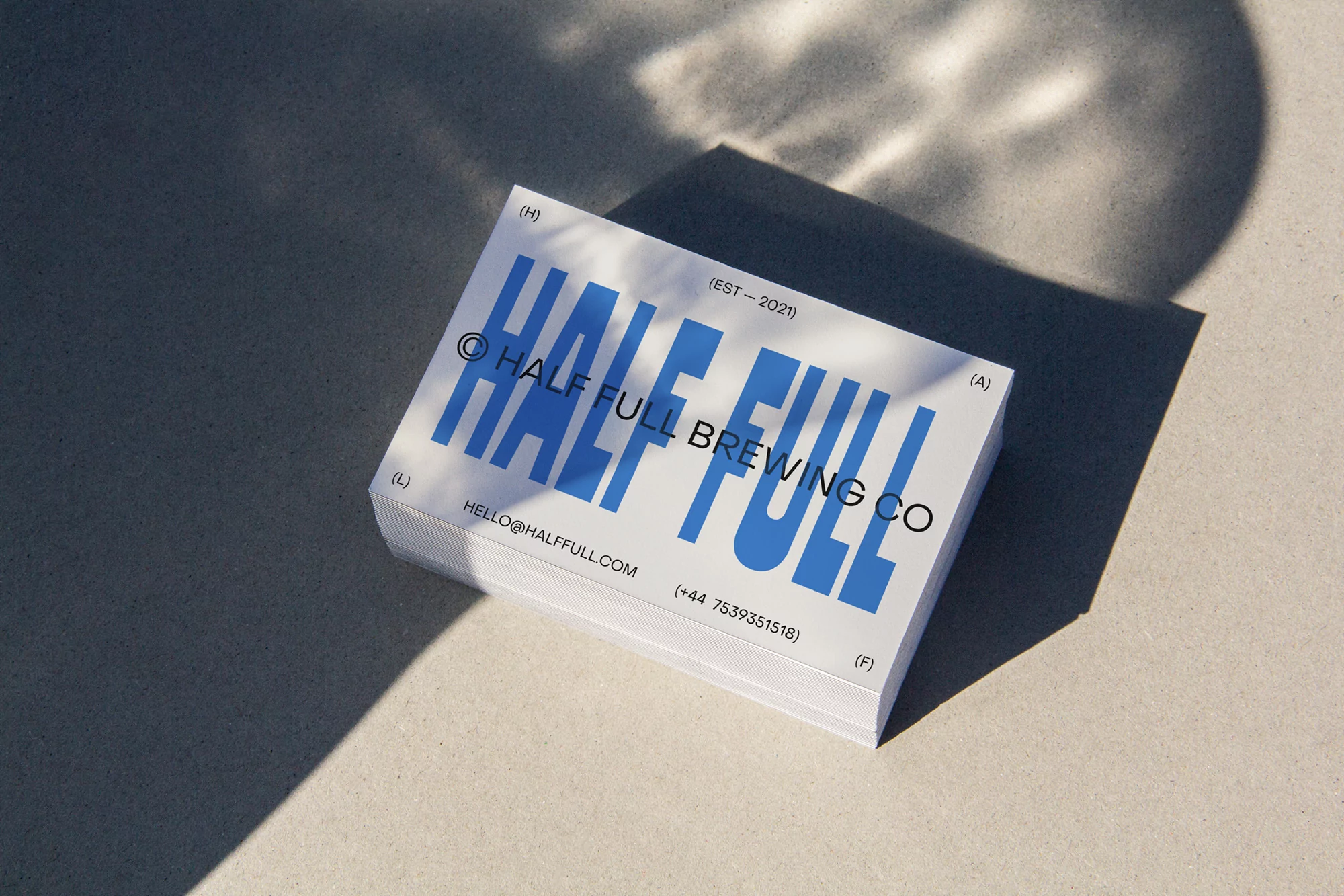 Stack of white business cards with bold blue Half Full Brewing Co typography on concrete