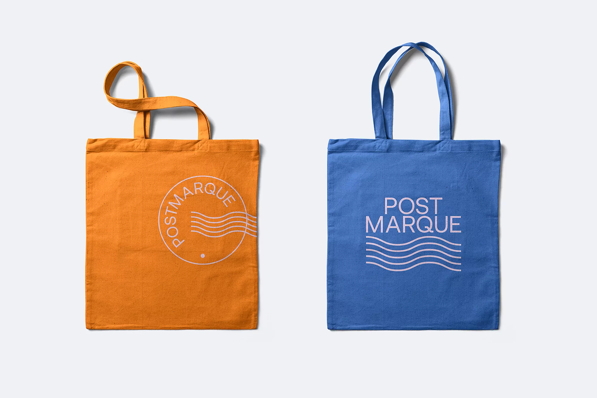 Two fabric tote bags, one orange and one blue, with a simple logo design, displayed on a clean white background in a studio setting.
