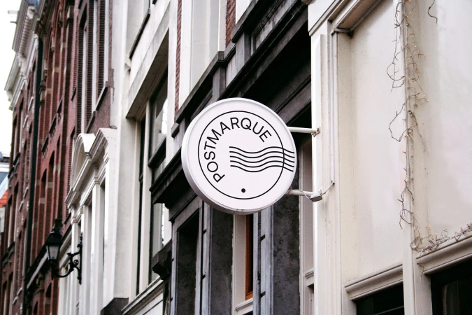 Round white Postmarque sign hanging on a historic European street building exterior