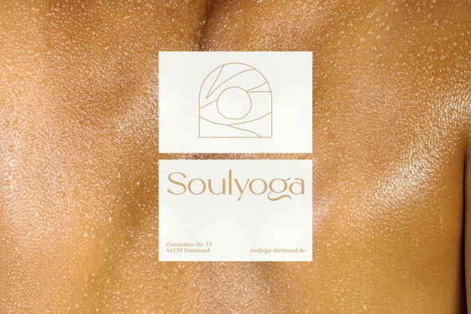 Close-up of a person's glistening skin with two stacked white cards displaying a gold logo and the text 'Soulyoga' and contact details.