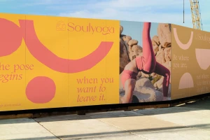 Soulyoga brand identity signage on construction hoarding featuring yellow panels with pink abstract shapes and typography.