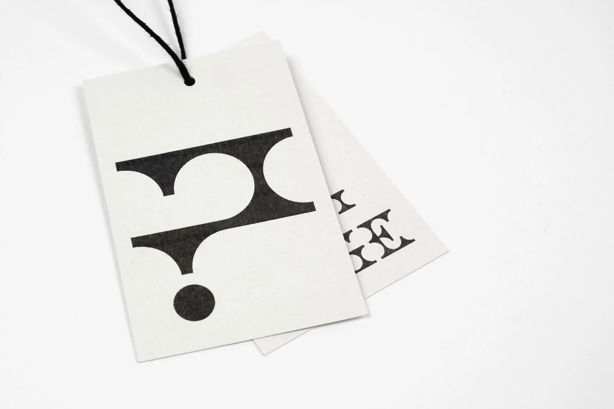 Two off-white tags with black logo and string on a white background in a close-up shot, for branding and product information.
