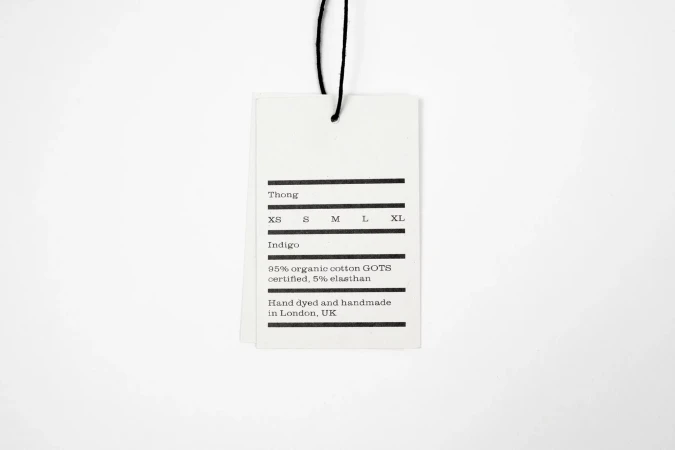 White paper clothing tag hanging from a black string against a clean, plain white seamless background.