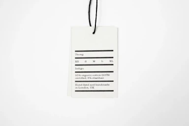 White paper clothing tag hanging from a black string against a clean, plain white seamless background.