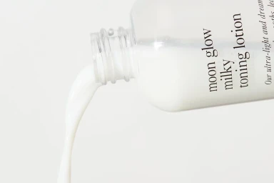 Clear plastic skincare bottle pouring white milky lotion against a seamless bright white background