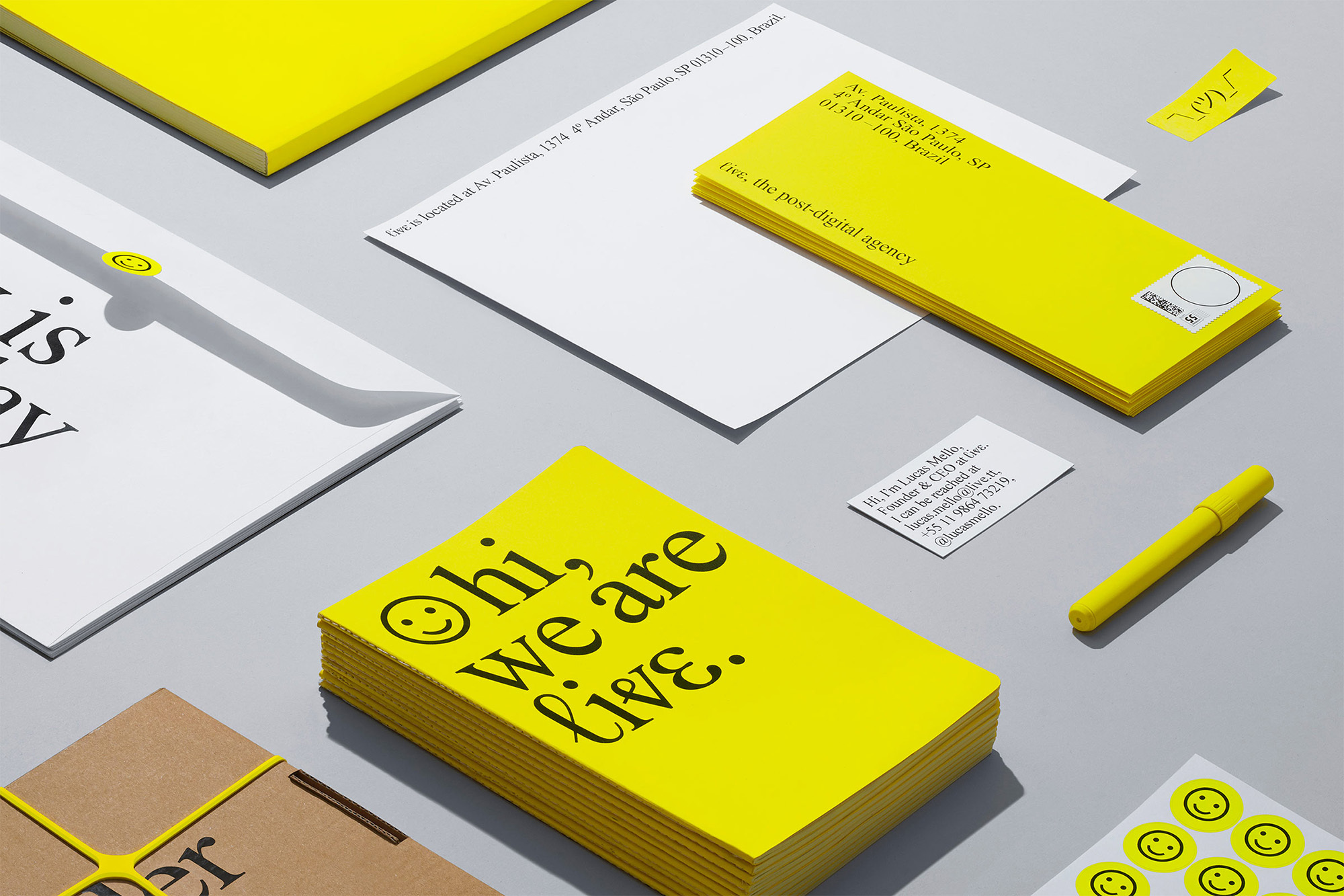 Overhead shot of yellow and white stationery including postcards, envelopes, stickers, and a pen against a gray surface.
