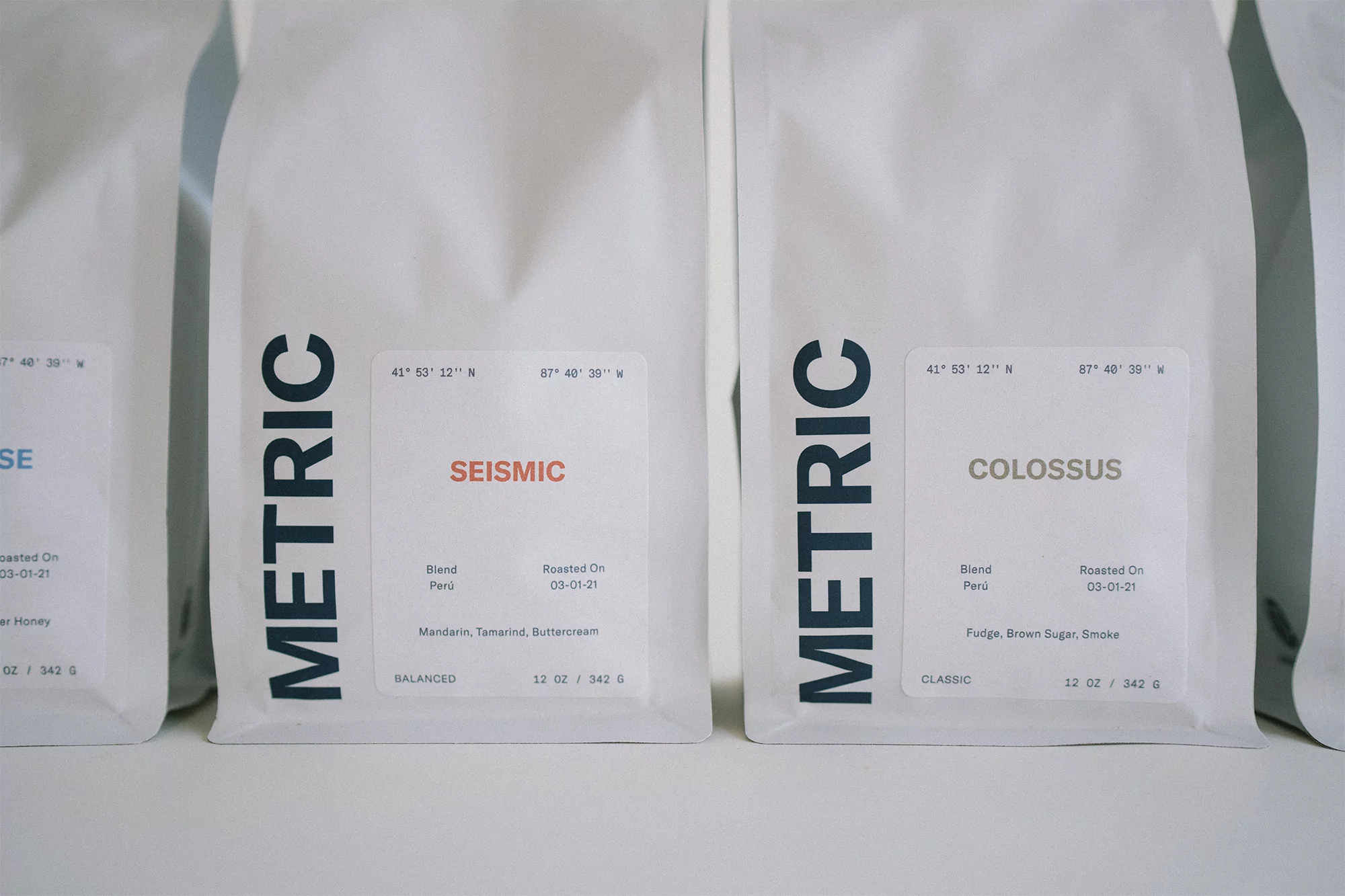 Close-up of white coffee bags from Metric Coffee with different roasts and flavor profiles, including Seismic and Colossus blends.