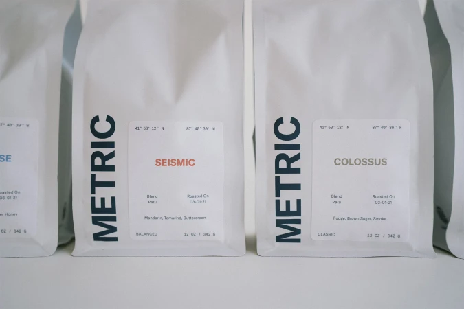 Close-up of white coffee bags from Metric Coffee with different roasts and flavor profiles, including Seismic and Colossus blends.
