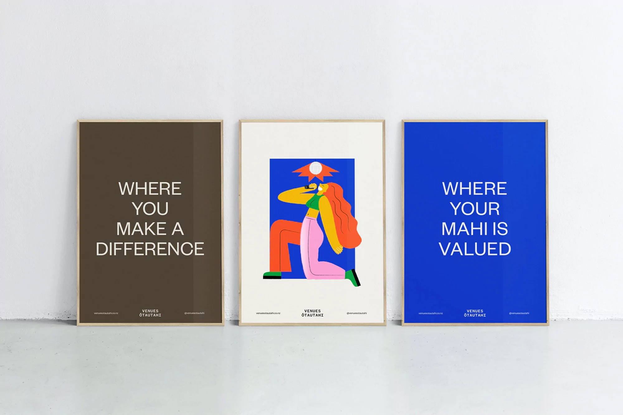 Three framed posters on a white wall with a concrete floor; one with brown background, one with illustration, one with blue background.