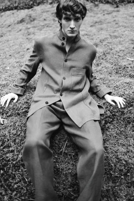 A model in a suit lies in grassy moss, showcasing a vintage black and white fashion editorial with a soft outdoor setting and natural lighting.