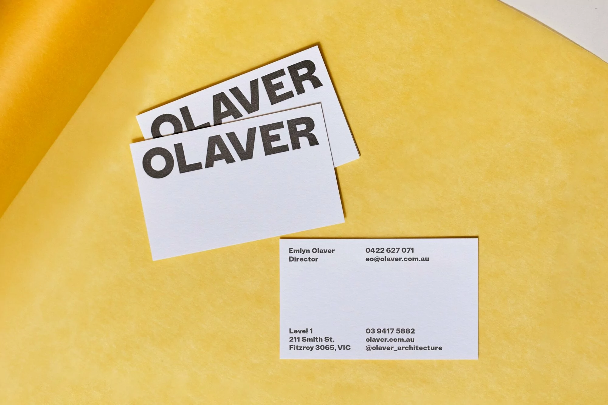 Elevated studio shot of three white business cards with black text on a yellow surface with professional and architectural details.