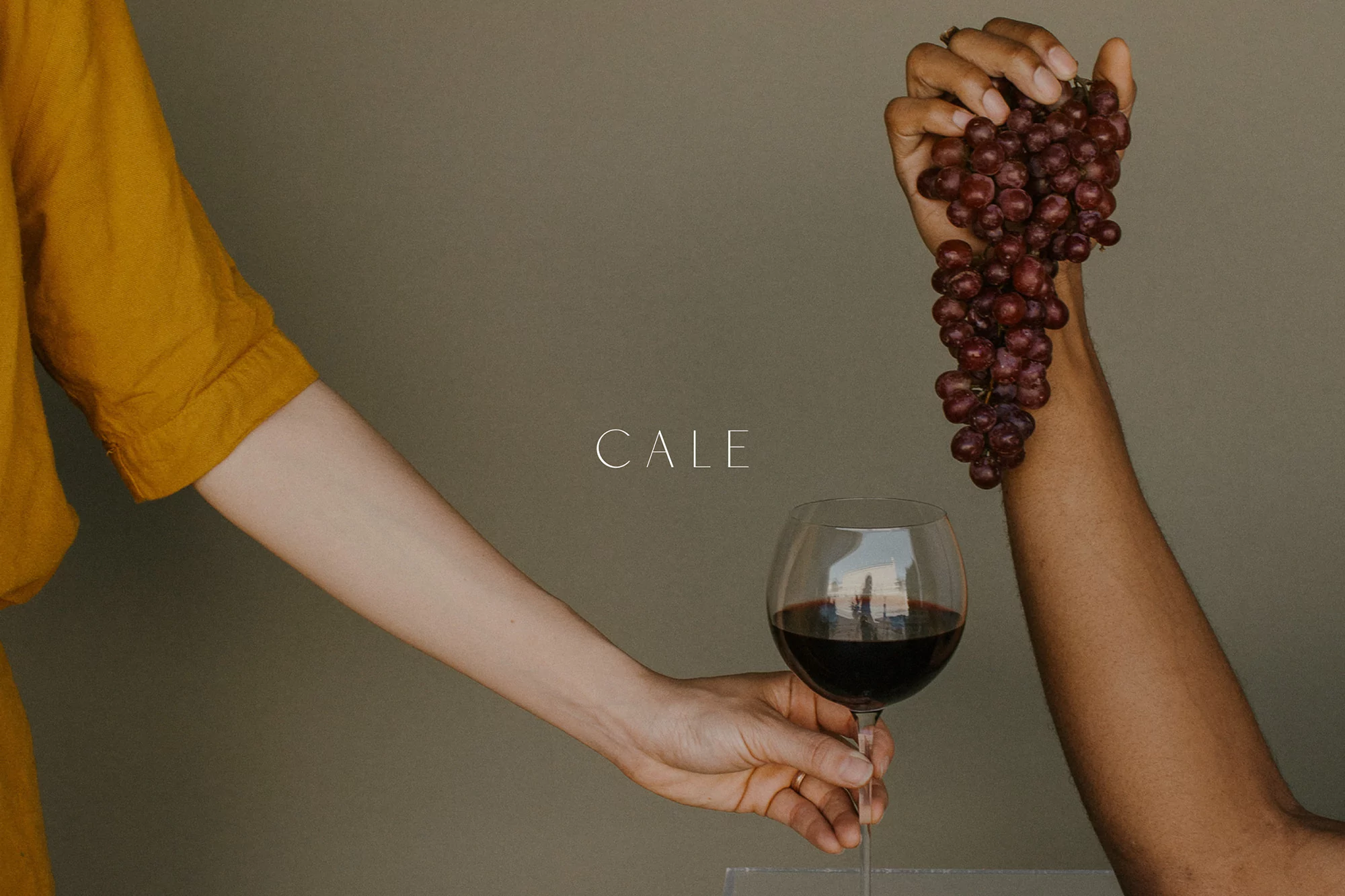 Close-up studio shot of a two hands, one holding wine glass with red wine and the other holding a bunch of red grapes.