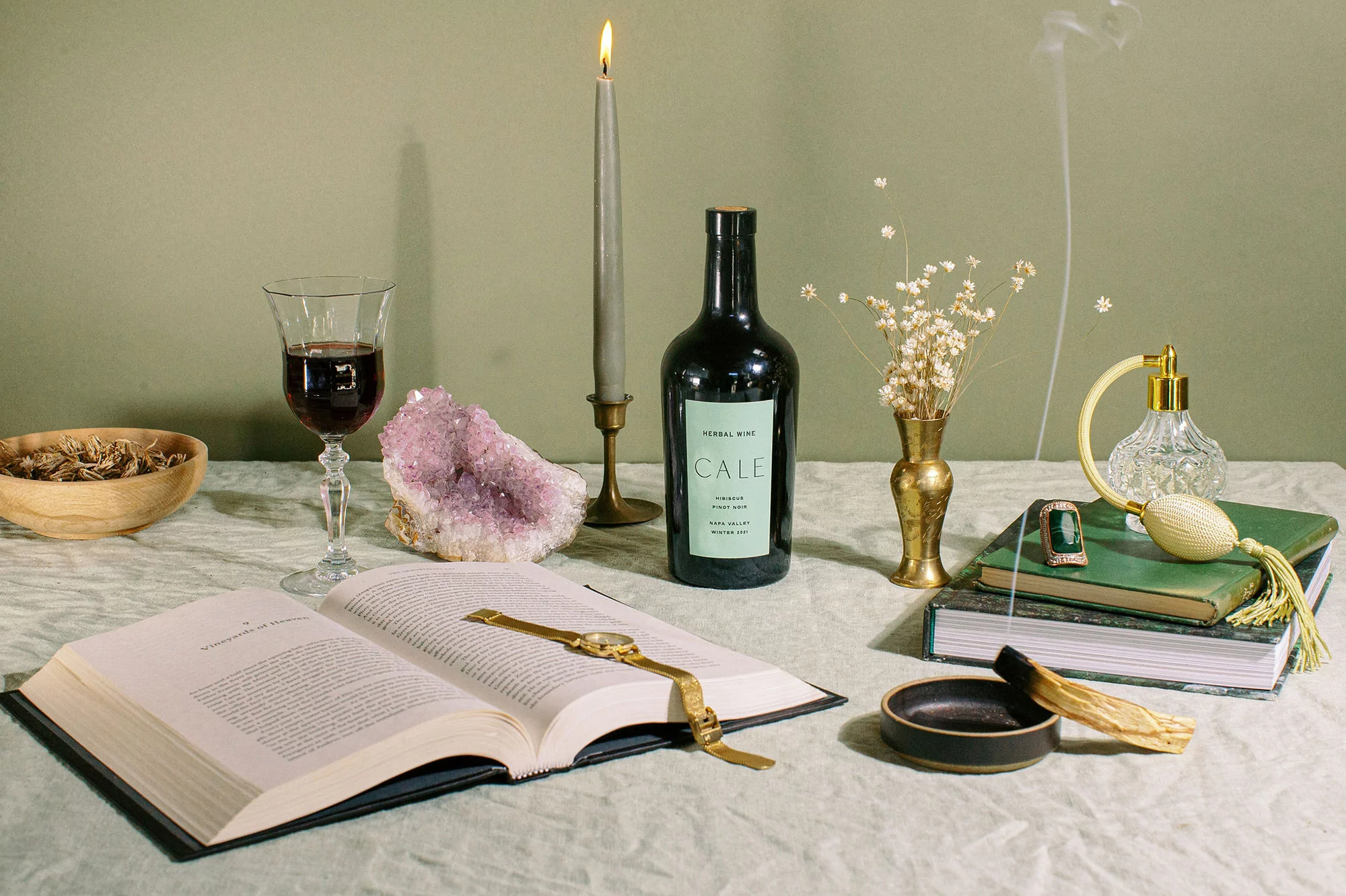 Still life composition featuring an open book, wine glass, candle, and wine bottle, arranged on a table with soft, muted lighting.