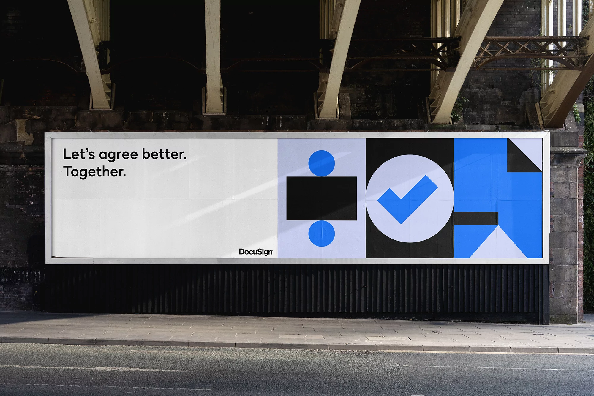 A large DocuSign billboard featuring text and abstract blue and black geometric shapes is displayed under a concrete overpass.