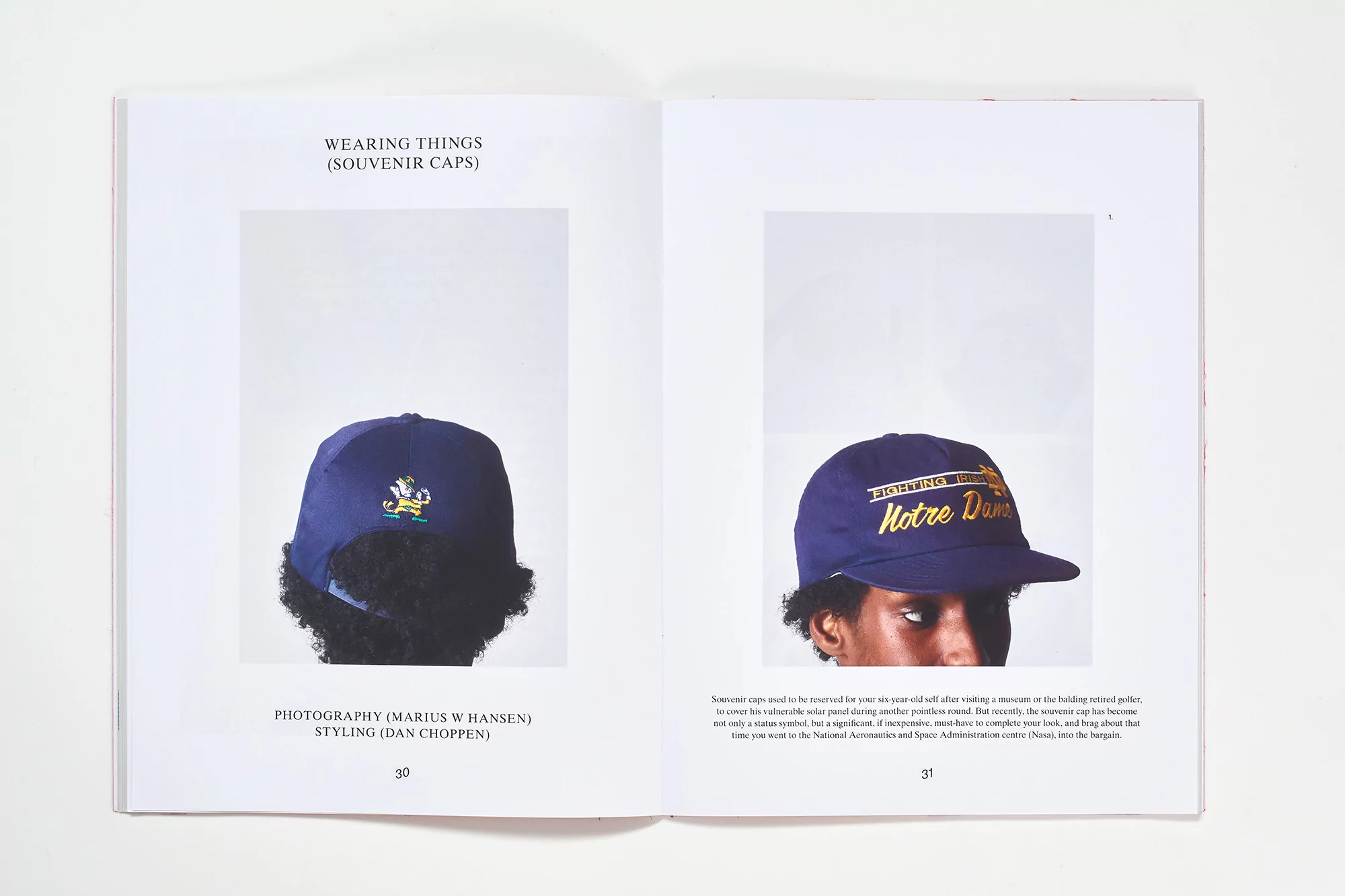 Two open magazine pages show navy blue baseball caps, one with a leprechaun logo, the other with gold 'Notre Dame' text, on white backgrounds.