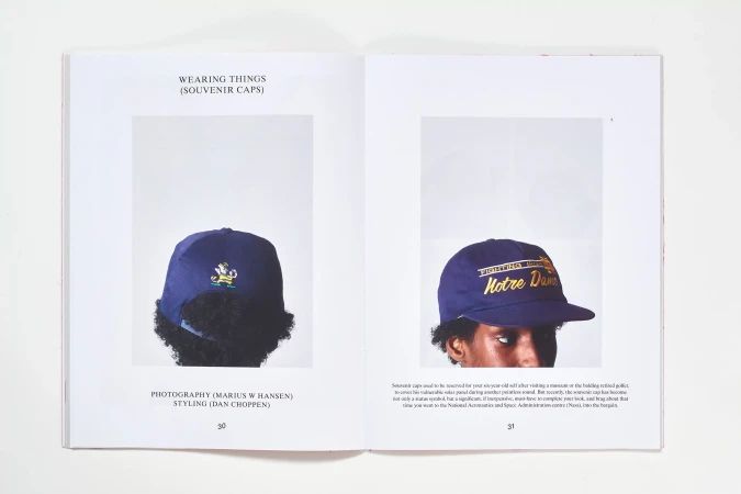 Two open magazine pages show navy blue baseball caps, one with a leprechaun logo, the other with gold 'Notre Dame' text, on white backgrounds.