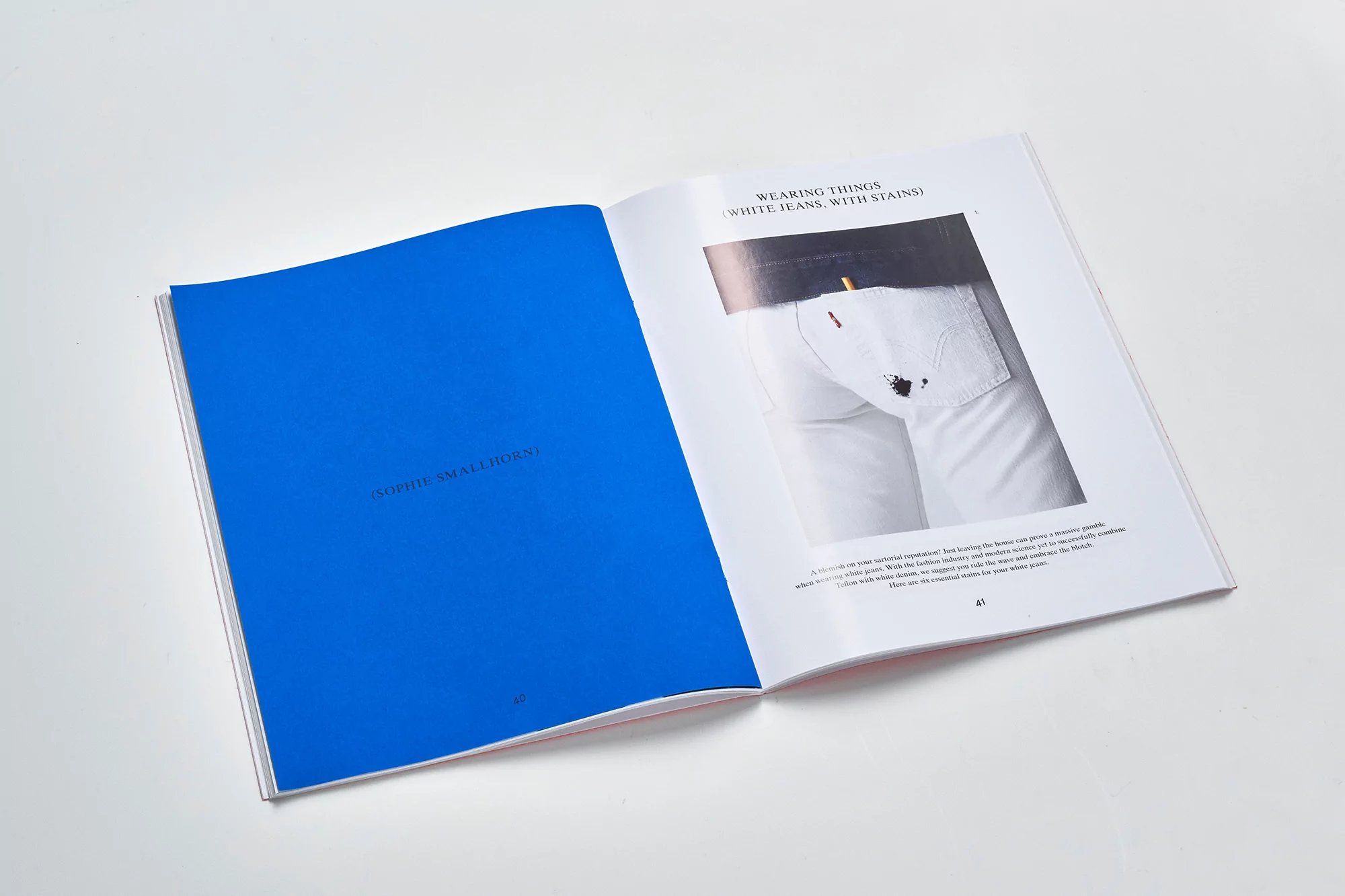 Open book with blue and white pages displays fashion editorial content featuring white jeans with stains in an indoor setting.
