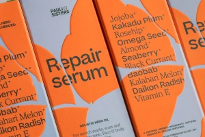 Close-up product packaging for Pauli & Sisters Repair Serum featuring embossed orange leaf shapes on pale blue boxes with typography.