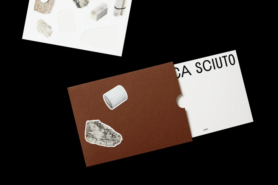 An envelope with a white card, and stickers of rock-like minerals adorn a piece of white paper, set against a black backdrop.