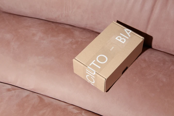 Branded cardboard shipping box resting on a pink textured leather sofa surface.