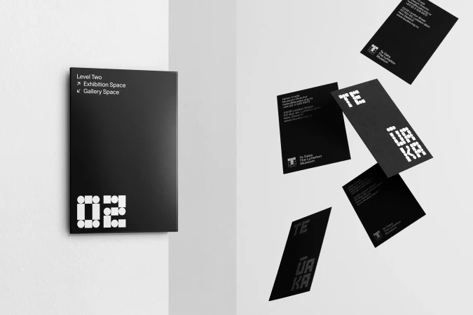 Black museum wayfinding sign and floating business cards with white dot-matrix typography against white walls