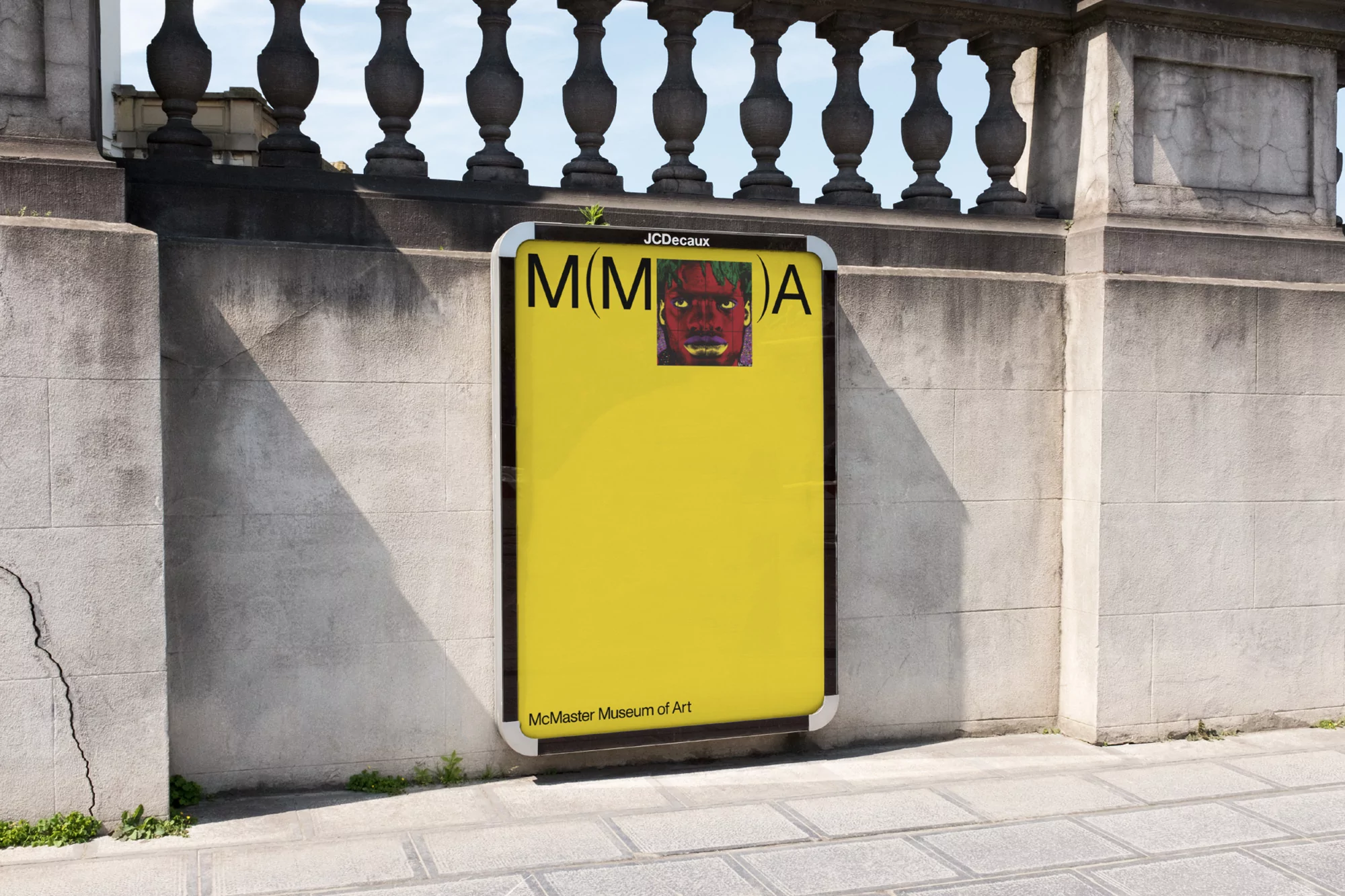 Outdoor advertising billboard featuring artwork for McMaster Museum of Art, mounted on a stone wall near a patterned sidewalk.