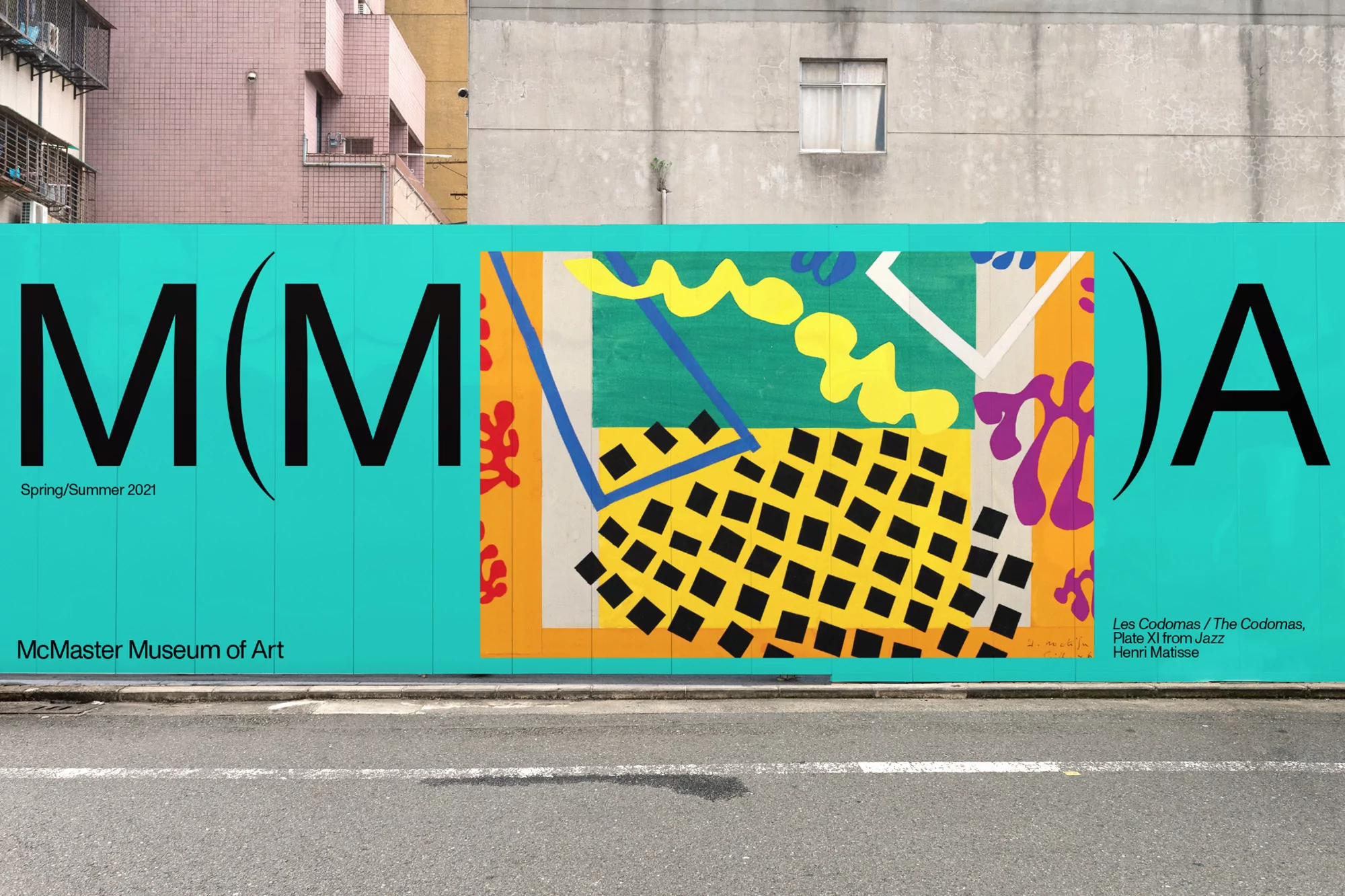 Street-level view of the McMaster Museum of Art promotion featuring vibrant abstract art on a blue hoarding next to a building.