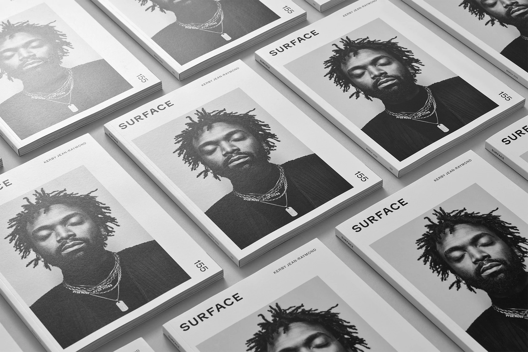 Several copies of SURFACE magazine featuring a portrait of a Black male model with dreadlocks and a necklace on a light gray background.