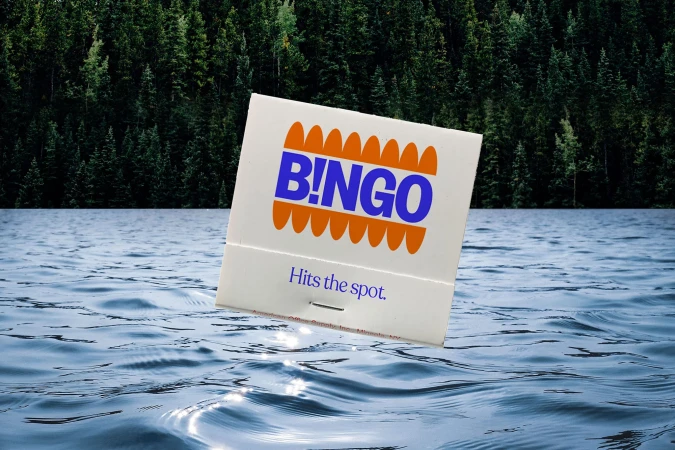 Matchbook floating on water with forest background. The matchbook is white with the word B!NGO in blue and orange design.