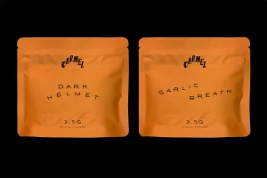 Two vibrant orange cannabis packaging pouches by Carmel brand against a plain solid black background.