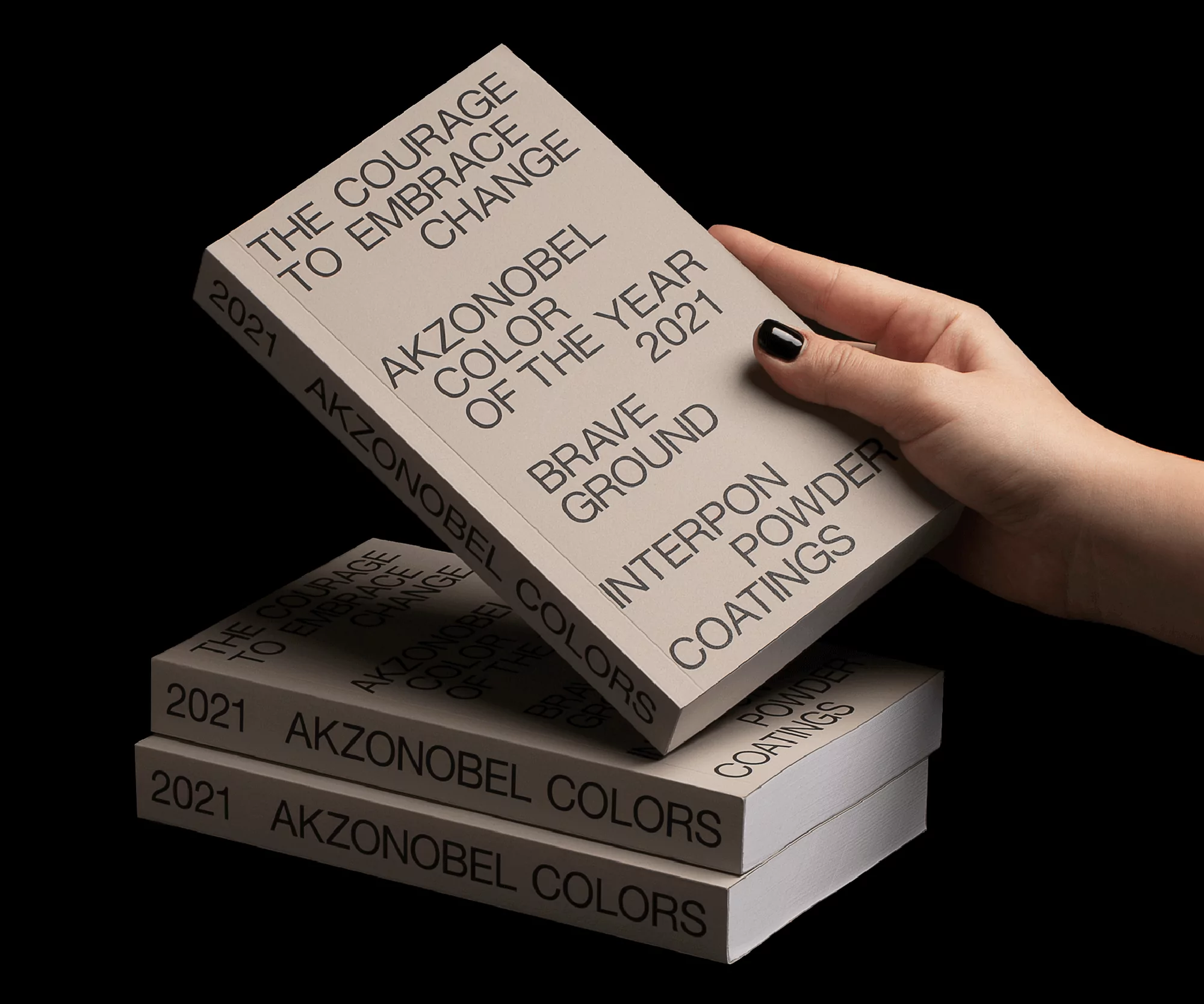Hand holding AkzoNobel 'Color of the Year 2021' book, with two stacked books beneath, set against a dark background. 