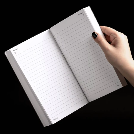 Open notebook with lined pages held by a hand against a black background, displaying blank pages for notes or scheduling.