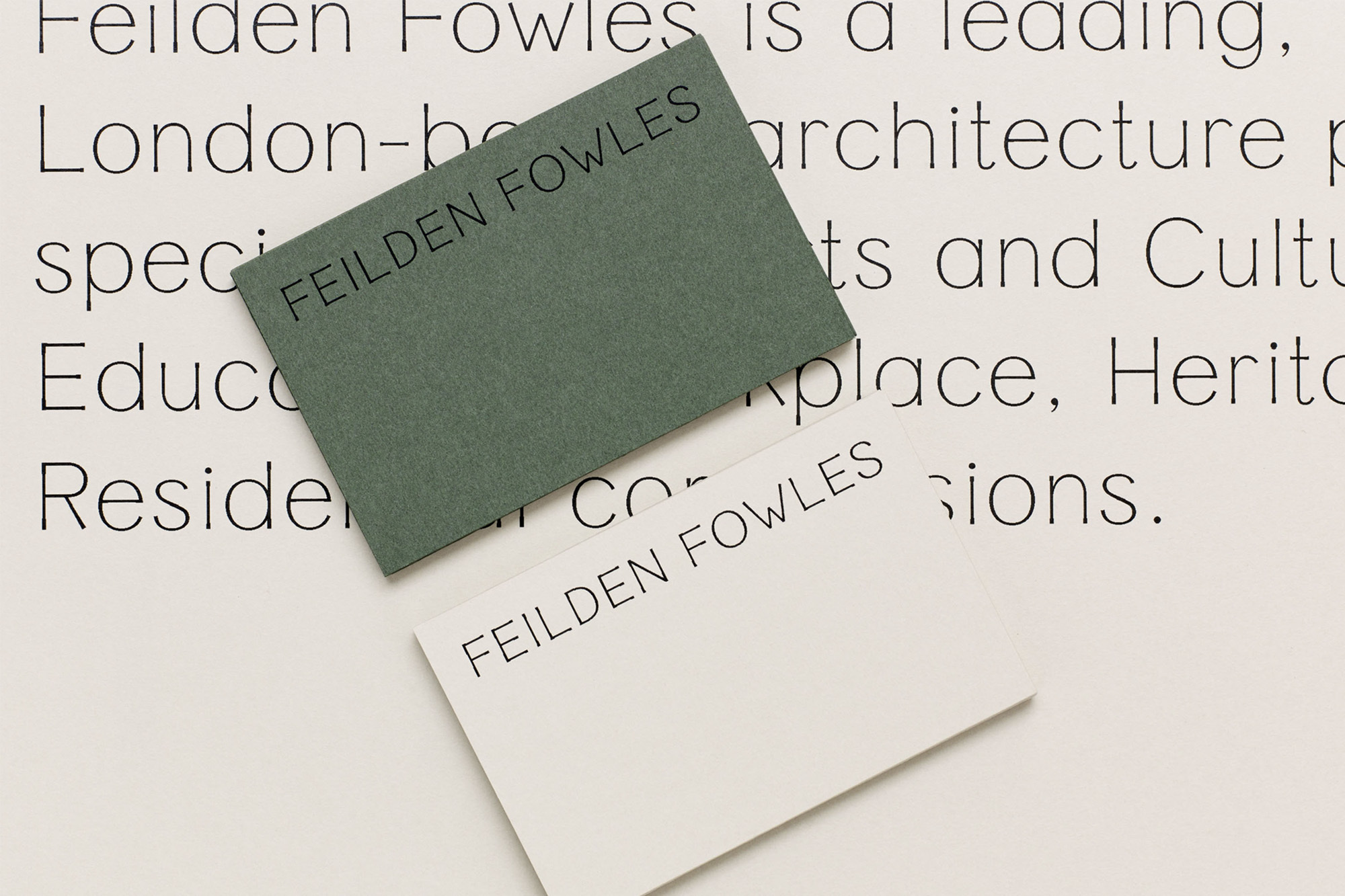 Two business cards, one green and one white, are diagonally placed on a background with printed architectural text, with a focus on design.
