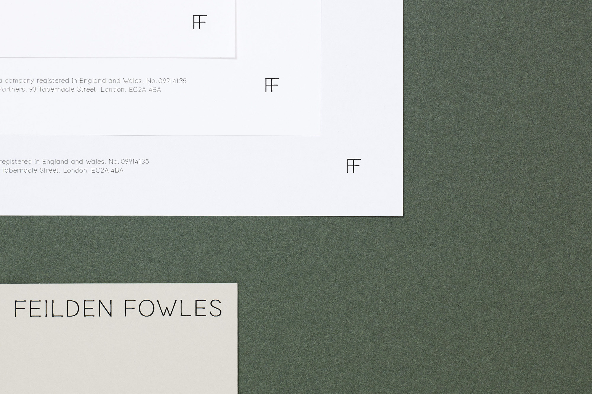 Close-up of Feilden Fowles company stationery with logo and contact information on white paper against a dark green background.