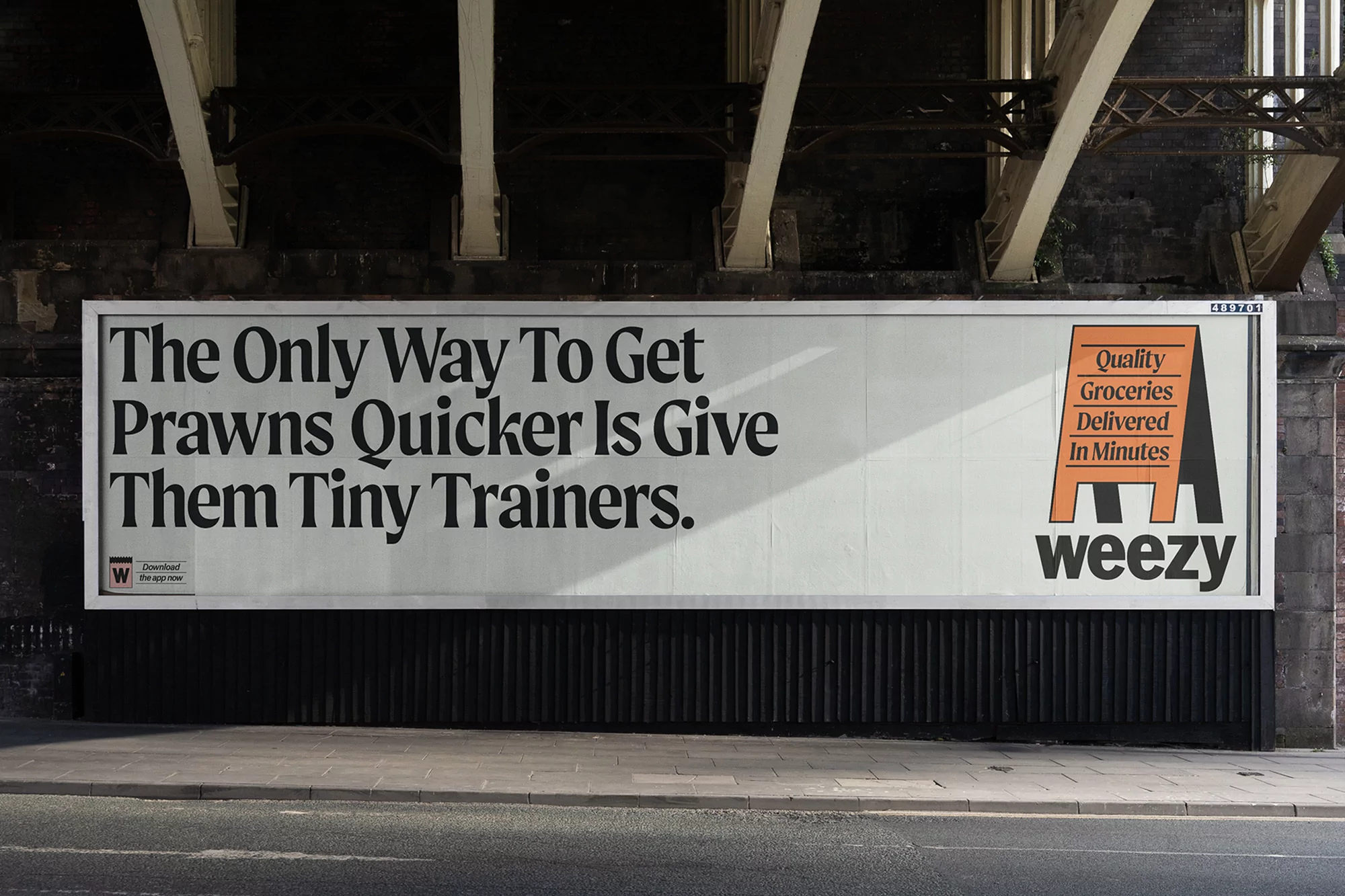 Eye-level view of a Weezly billboard with a black background and a cream-colored billboard with black and orange text, promoting grocery delivery.